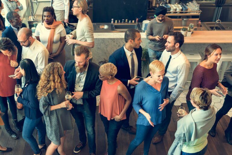 Diverse group of people socializing at a modern event, enjoying drinks and engaging in conversation in a lively atmosphere.