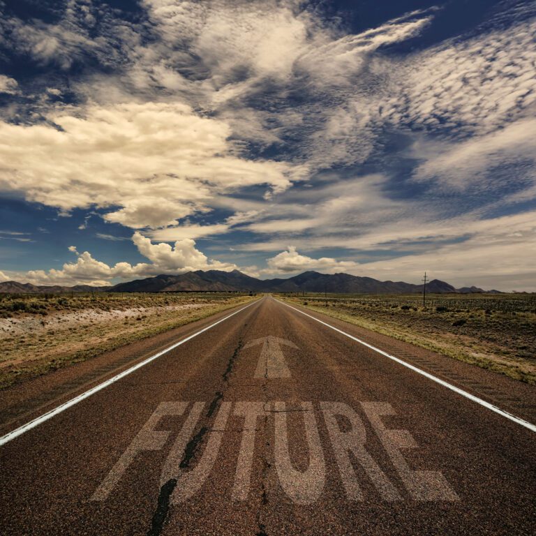 A long, empty road stretches toward distant mountains under a dramatic sky, with the word "FUTURE" marked on the pavement, symbolizing progress.