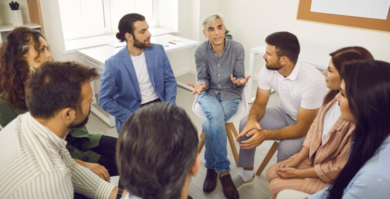 Senior coach having conversation with team of business people or company employees