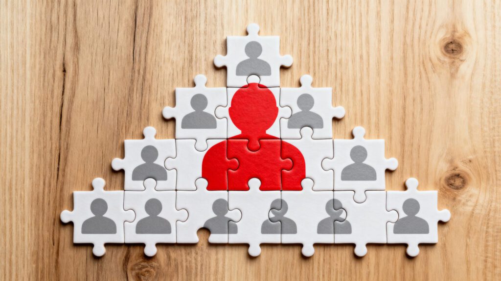 Puzzle pieces with red person symbol on wooden background, leadership concept