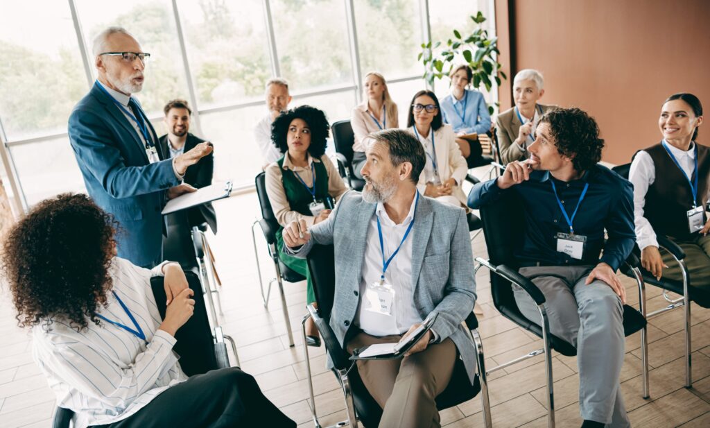 Senior speaker presenting to a diverse group of professionals at a business seminar or workshop.